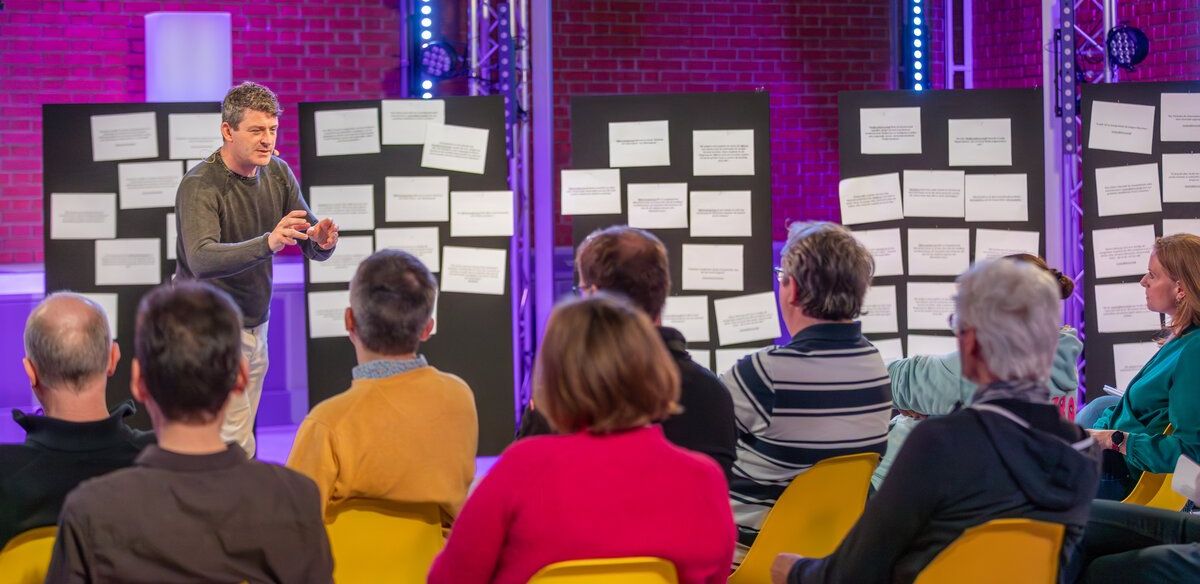 Alexis Johann moderiert eine Beteiligungssession vor Thesenwänden